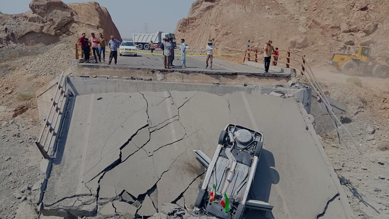 An overturned car sits on a section of a destroyed bridge after a strike in Hormozgan...