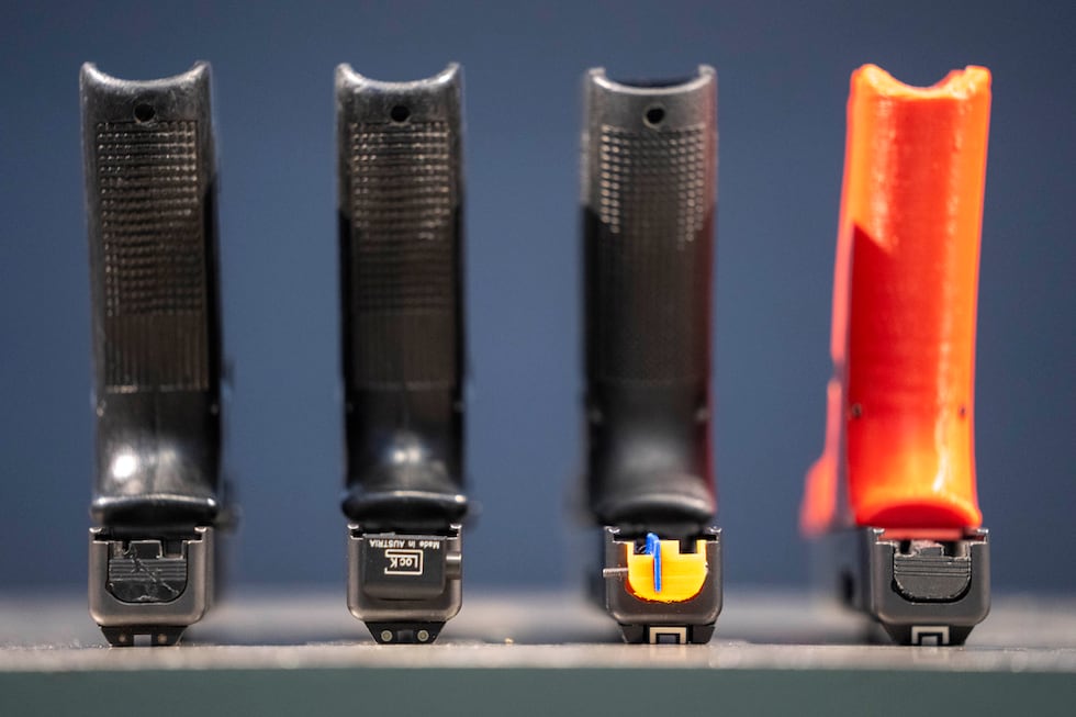 A row of semi-automatic pistols is displayed, some with conversion devices that make them...
