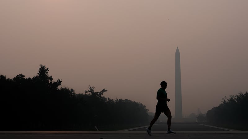The sun is obscured by wildfire smoke as a person runs in front of the Washington Monument and...
