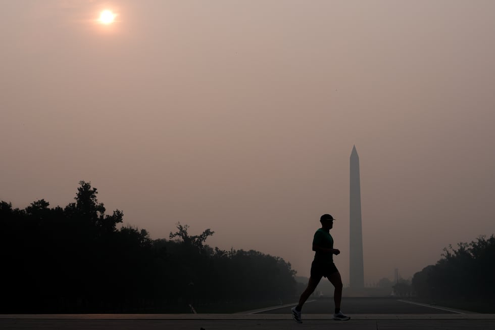 The sun is obscured by wildfire smoke as a person runs in front of the Washington Monument and...