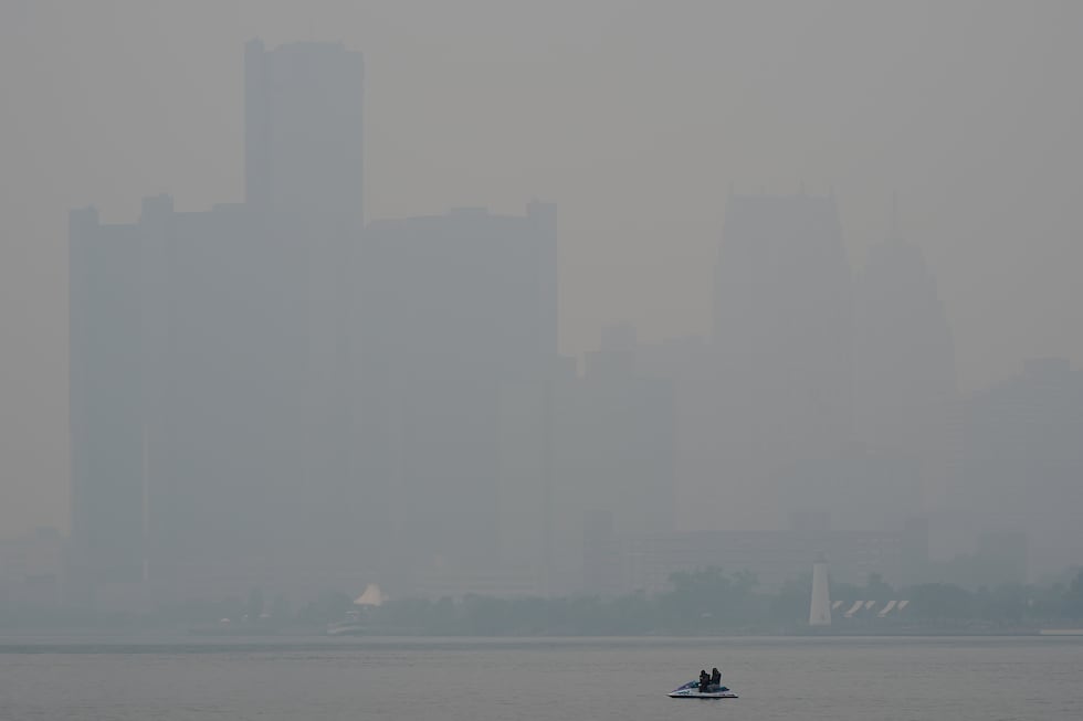 A watercraft sits in the Detroit River near the skyline during poor air quality due to smoke...