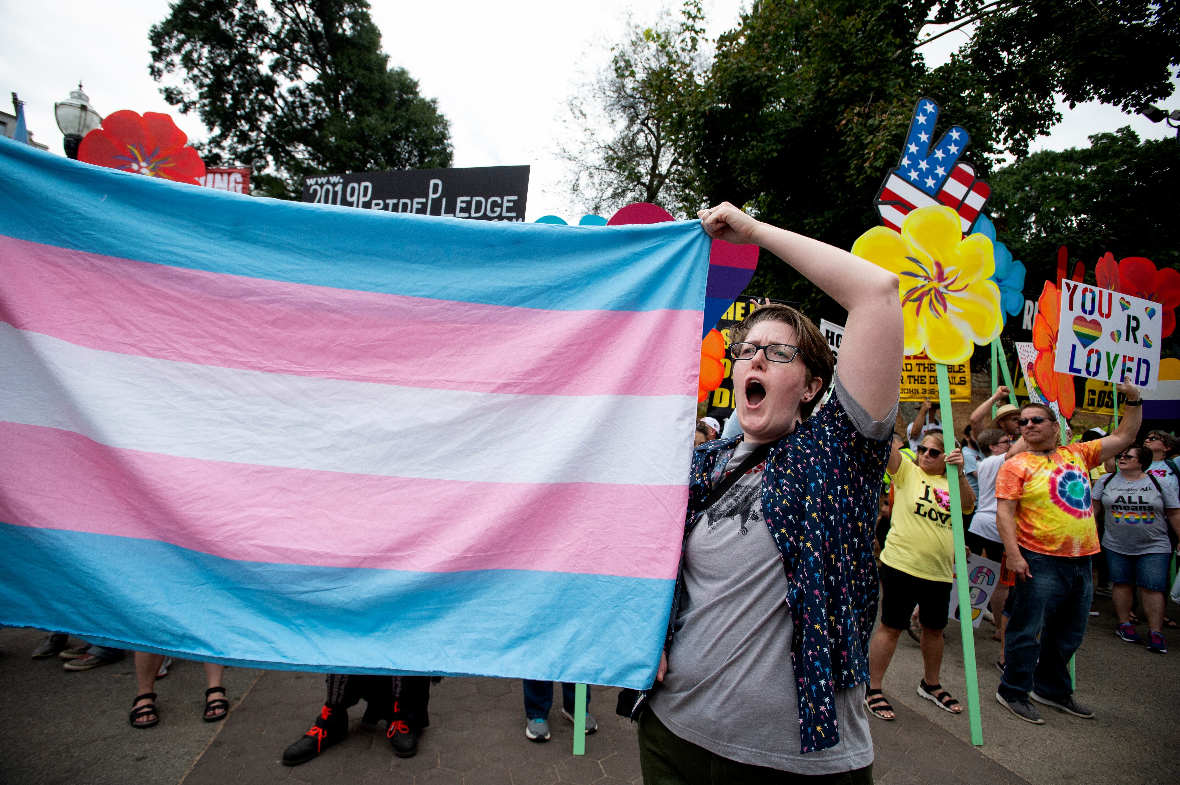 FILE - A er for the transgender community holds up a flag in front of...